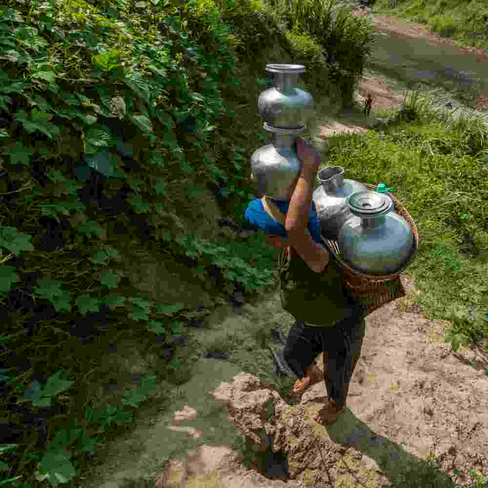 A woman carrying the heavy load of pots full of water on her head and in a basket all the way from the river back to her village house.