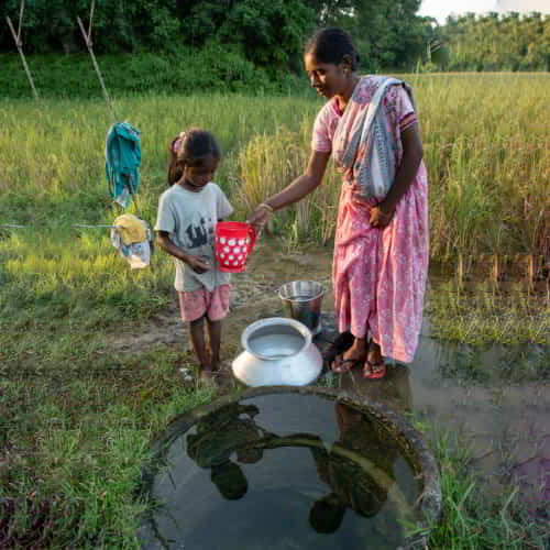 Mother and child in poverty collecting contaminated water from an open well