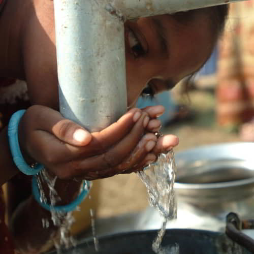 Young girl enjoys drinking water through Jesus Wells by GFA World, a clean water Christian organization