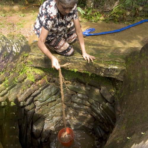 Woman drawing unclean water from an open water well